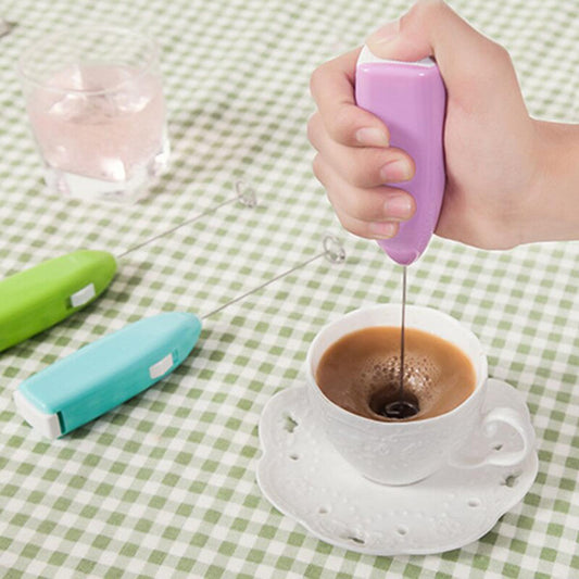 Close-up of a handheld electric milk frother whisking milk into a rich, creamy foam in a clear glass mug.