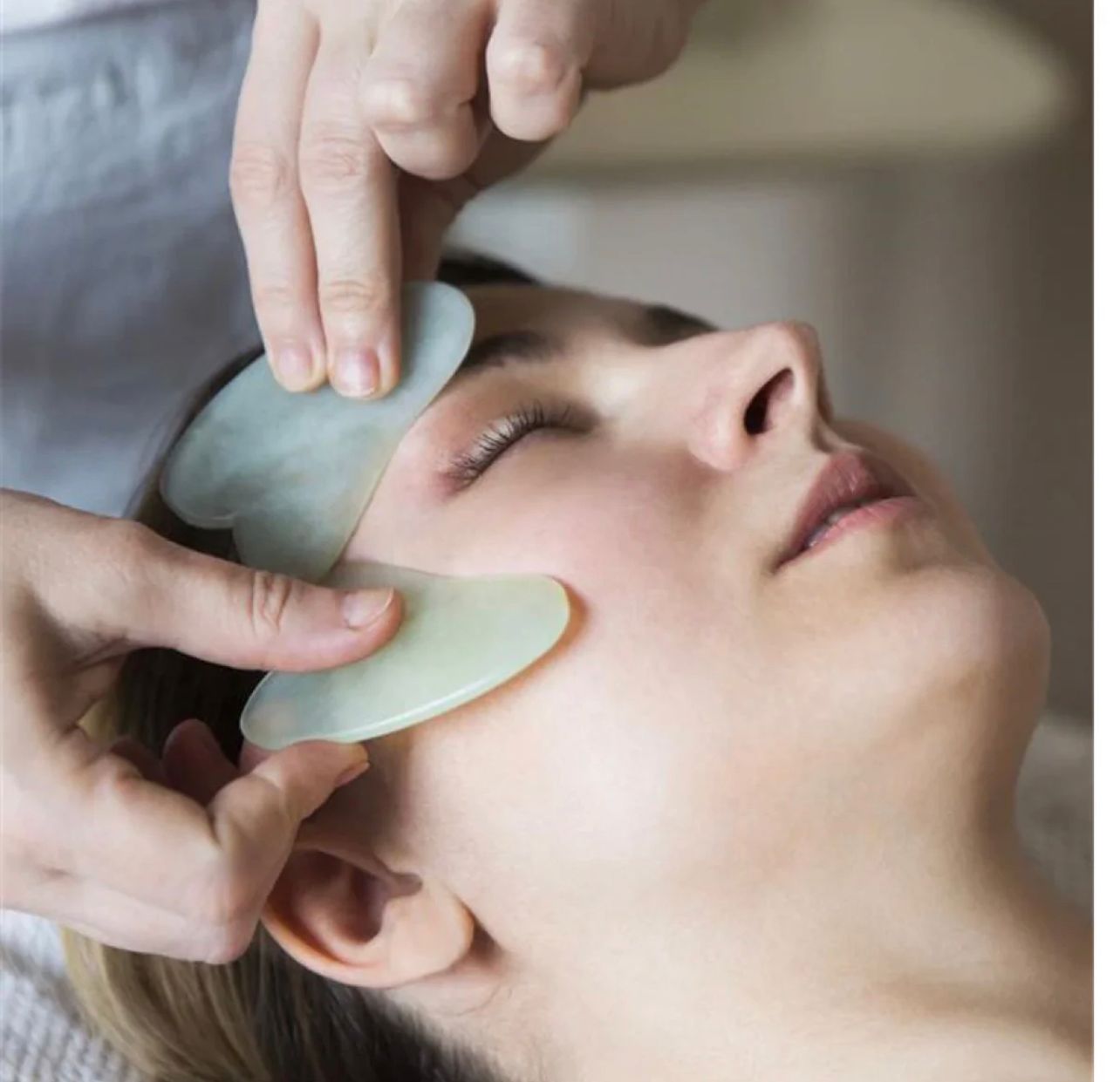 Close-up of a woman scraping her jawline with a green jade gua sha tool for facial lifting and contouring.