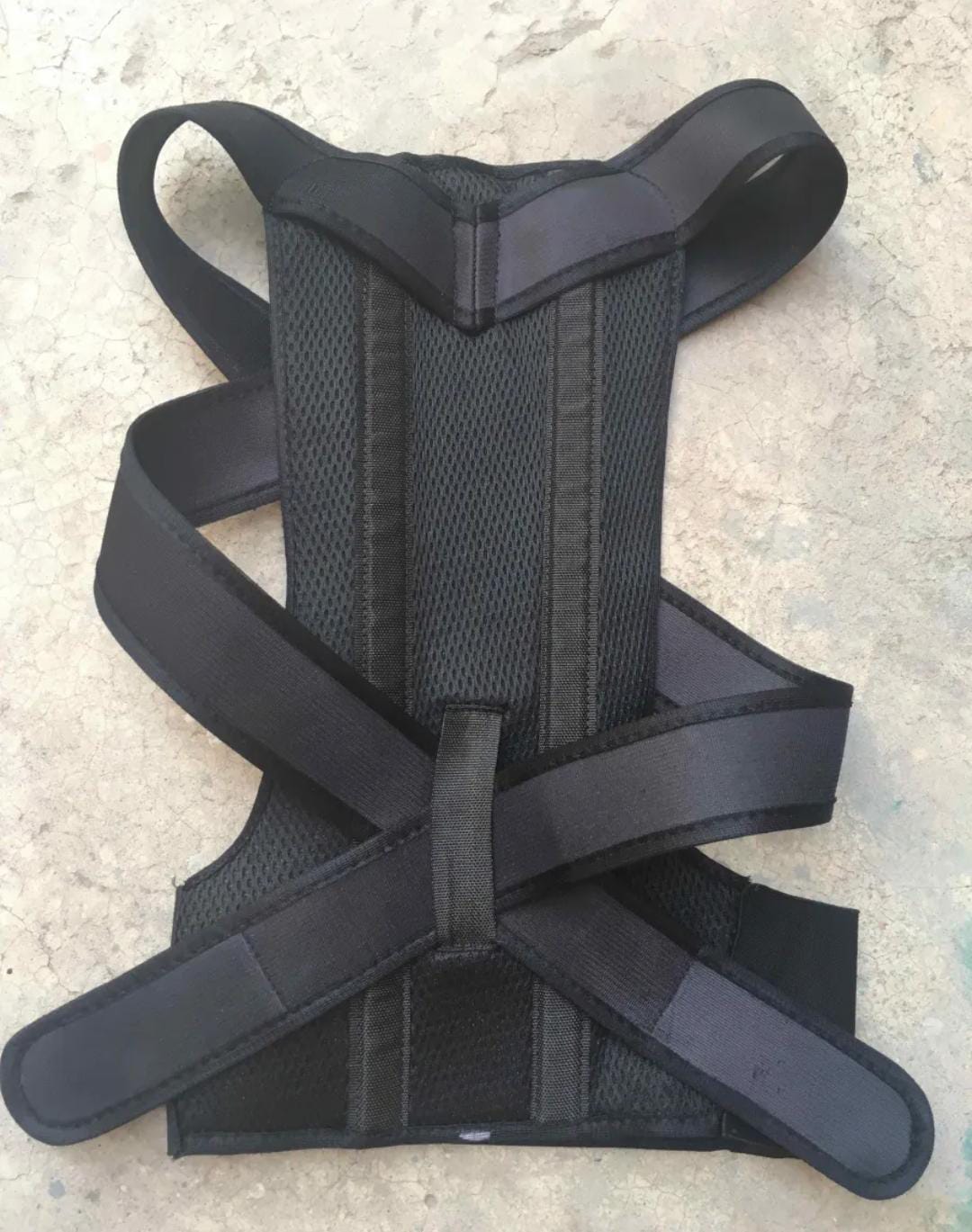 Close-up of a man wearing a black adjustable posture corrector belt over his t-shirt to fix rounded shoulders and hunchback.